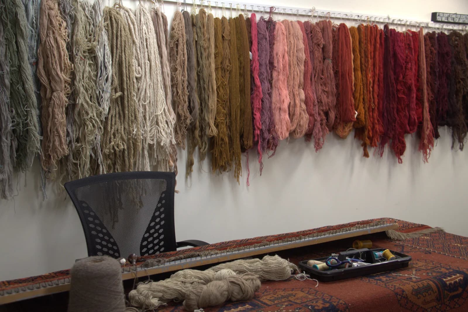 Hand-dyed wool skeins on the colour-matching wall above a repair workbench at Ahmadi Rug's Skokie workshop